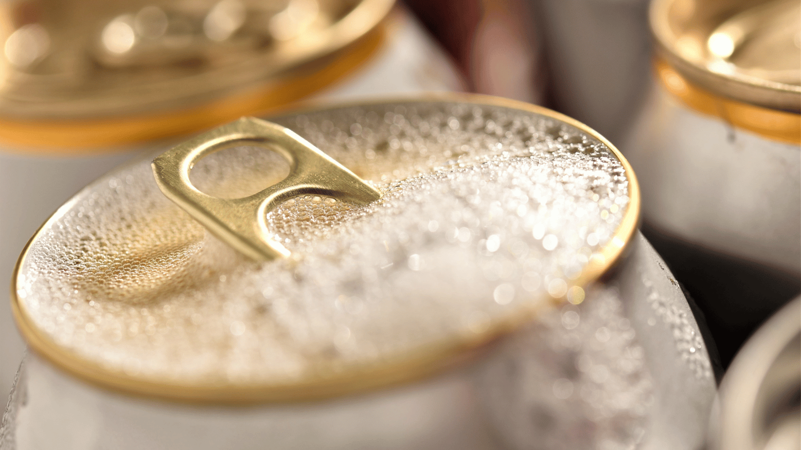Close-up of a can of carbonated drink with the tab partially lifted and the liquid coming out the top.