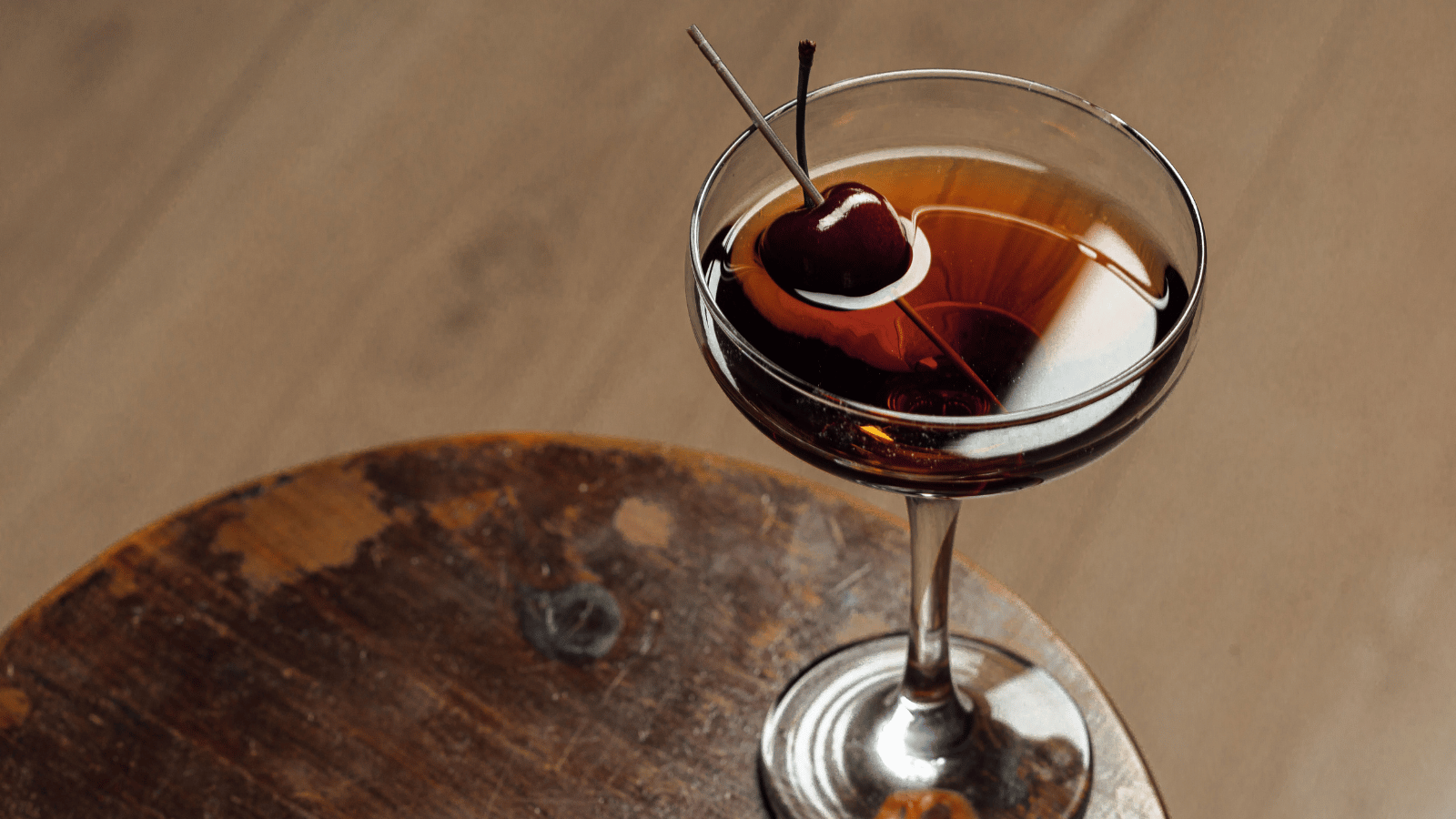 A negroni in a tulip glass with a cherry garnish on a wood table
