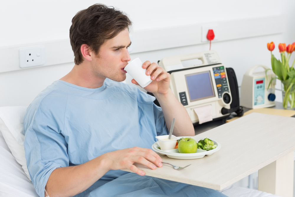 Young male patient drinking water while having meal in hospital